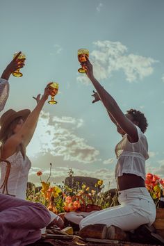 two women sitting on the ground holding wine glasses in their hands and toasting with each other