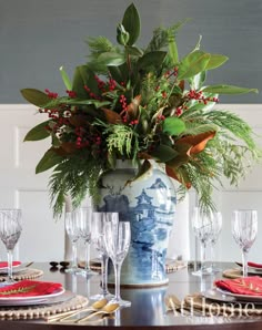 a blue and white vase filled with greenery on top of a wooden dining table