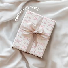 a gift wrapped in pink and white wrapping paper with a bow on the top, laying on a bed