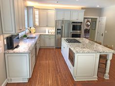 a kitchen with white cabinets and marble counter tops, hardwood floors, and stainless steel appliances