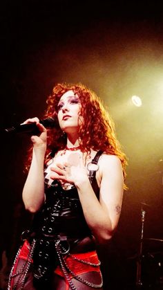 a woman with red hair is holding a microphone in her hand and singing into the microphone