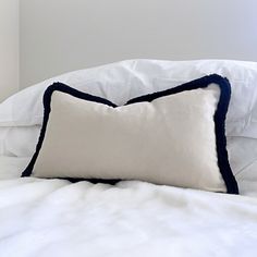 a white and blue pillow sitting on top of a bed next to a white blanket