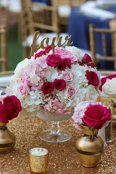 pink and white flowers sit in vases on a table with gold candlesticks