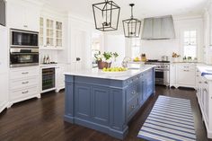 a kitchen with white cabinets and blue island in the center, surrounded by hanging lights