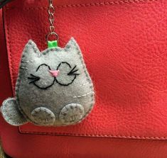 a gray cat keychain hanging from a red leather bag with a green tag on it