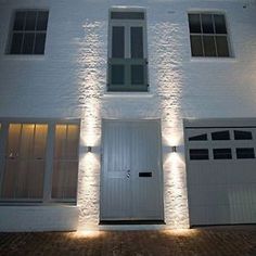 a white house with two garage doors and lights on the side of it at night