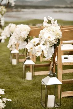 white flowers and candles are lined up along the grass at an outdoor ceremony with wooden benches