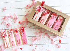 pink and red candles in a box on white wooden table with confetti scattered around