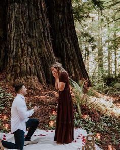 a man kneeling down next to a woman on a blanket in front of a tree