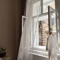 an open window with white sheer curtains and clothes hanging on the rack next to it