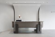 a man sitting at a desk with a laptop on top of it in front of a white wall