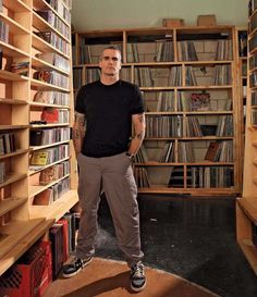 a man standing in front of a bookshelf full of cds and dvds,