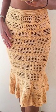 a woman wearing a yellow crochet skirt with her hands on her hips and holding a cell phone