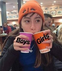 a girl holding two cups with the words boys and girls on them in front of her face