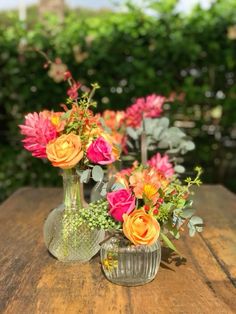 two vases filled with colorful flowers sitting on top of a wooden table next to each other