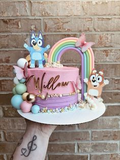 a person holding up a cake decorated with cartoon characters and the word welcome on it