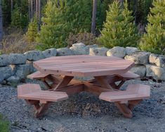 a wooden picnic table sitting on top of a gravel field next to some rocks and trees