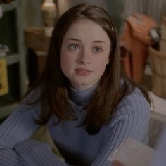 a young woman sitting on top of a bed next to a lamp and bookshelf