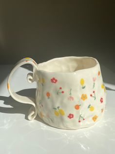 a white cup with flowers painted on it's side sitting on a counter top