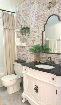 a bathroom with brick wall and white fixtures, black countertop sink, toilet and mirror