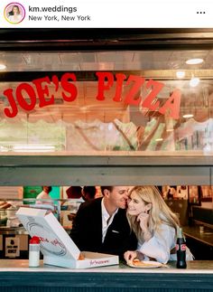 a man and woman sitting at a table in front of a pizza shop with the sign joe's pizza