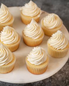 cupcakes with white frosting are arranged on a cake plate, ready to be eaten