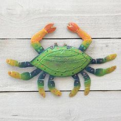 a green and yellow crab with two orange crabs on it's back, sitting on a white wooden surface