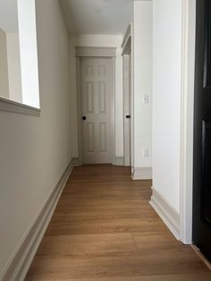 an empty hallway with hard wood floors and white trim on the door, along with two black doors