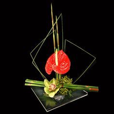 a vase with flowers and bamboo sticks on a black table top in front of a black background