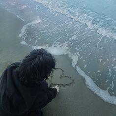 a person sitting on the beach writing in the sand with a heart drawn in the sand