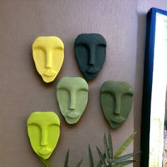 four different colored masks are on the wall next to a potted plant and window