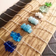 four sea glass necklaces sitting on top of a wooden board