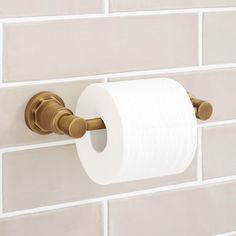 a roll of toilet paper hanging on a wall next to a white brick wall with gold handles