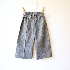 a pair of gray pants hanging on a white wall next to a wooden hanger