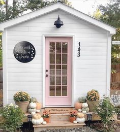 a small white house with pink door and window on the front porch, surrounded by potted plants