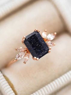 a black diamond ring sitting on top of a white velvet cushioned box with gold accents