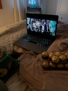 an open laptop computer sitting on top of a bed next to some chocolate covered cookies