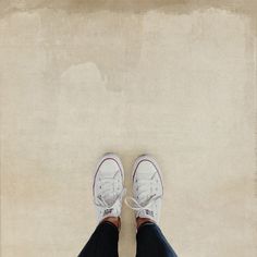 a person wearing white sneakers and jeans standing in front of a wall