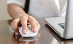 a person using a computer mouse at a desk with a laptop in the back ground