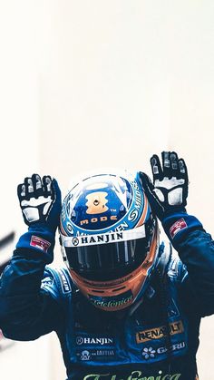 a man with his hands up in the air while wearing a racing suit and helmet