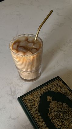 a drink in a glass next to a book on a table with a gold spoon