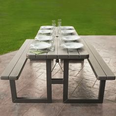 a long table with plates on it sitting in the middle of a patio next to a grassy field