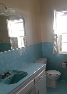 a bathroom with blue tile walls and flooring next to a white toilet under a window