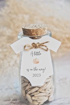 a small glass jar filled with lots of white sand next to a tag that says a little is on the way