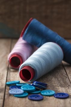 two spools of thread sitting on top of a wooden floor next to buttons