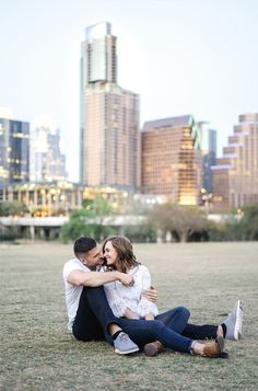 a man and woman sitting on the ground in front of a city skyline