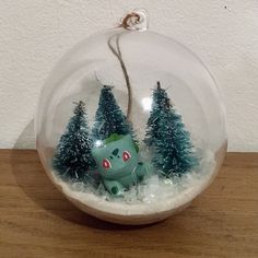 a snow globe with trees and a pokemon figure in it on a wooden table next to a white wall