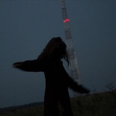 a person standing in the dark with their arms spread out, looking up at a tower