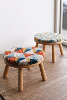 two small stools sitting on top of a wooden floor next to a glass window