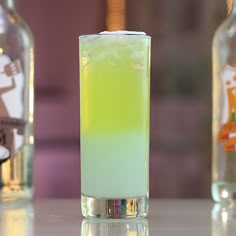 a tall glass filled with green liquid next to two empty bottles on a counter top